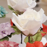 Auf dem Bild sind drei wei´ße Rosen , eine Mohnblume und eine Hortensiendolde in der Farbe Weiß-Rot zu sehen. Die Blüten sind aus essbarer Blütenpaste modelliert und stecken in einem Styroporkissen.